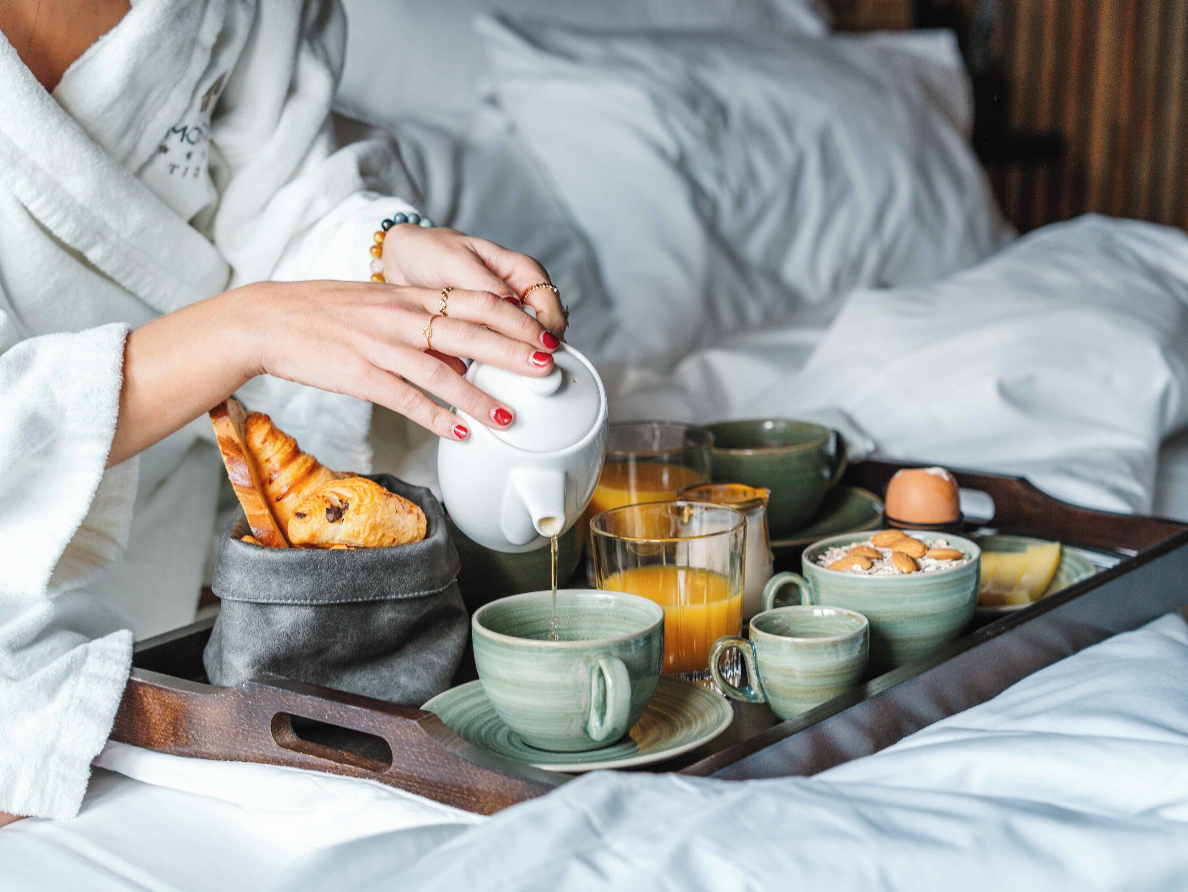Un plateau de petit-déjeuner avec du pain, des œufs et du jus d’orange, posé sur un lit.