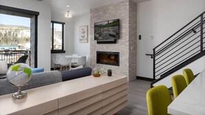 A modern living room with a fireplace, a flat-screen TV, a globe, and a staircase.