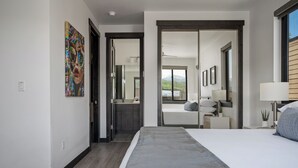 A modern hotel room with a large bed, a walk-in closet, a bathroom, and a view of the outdoors.