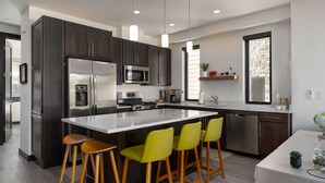 A modern kitchen with dark cabinets, stainless steel appliances, a central island with bar stools, and pendant lighting.