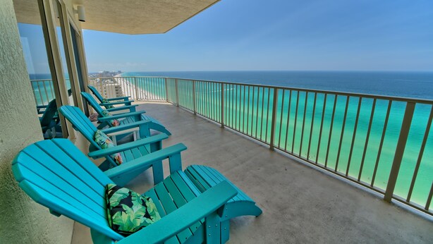 A balcony with turquoise chairs and a view of the ocean.