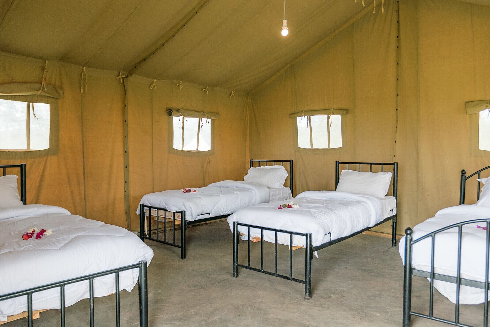 A room with four beds arranged in a square layout, each with white bedding and metal frames.