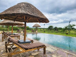 A pool area with lounge chairs and thatched umbrellas. - Africa Safari Serengeti Ikoma (Serengeti)