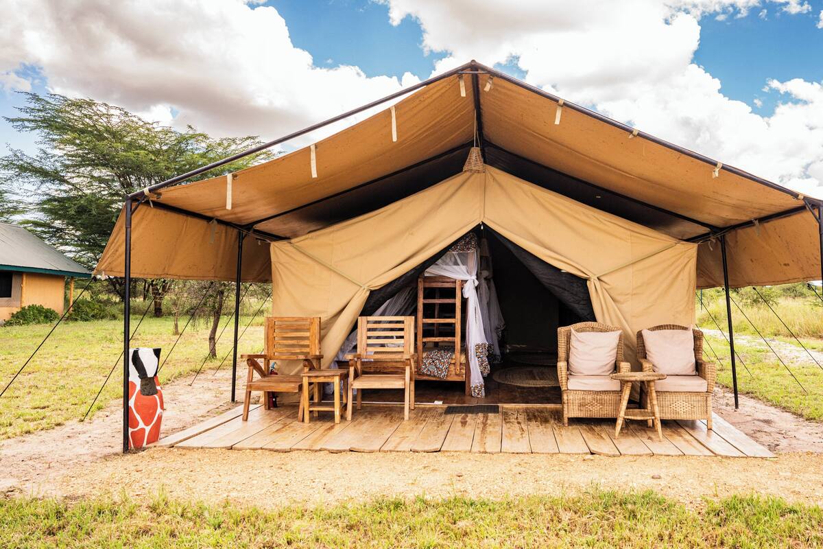 A tent with a wooden deck, two wicker chairs, and a ladder leading into the tent.