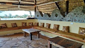 A thatched-roof outdoor seating area with a stone floor, a bench, and a table.