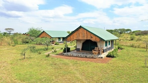 A lodge with a green roof and wooden exterior, surrounded by a grassy landscape with trees.
