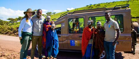 A group of people standing in front of a safari vehicle with a grassy landscape in the background.
