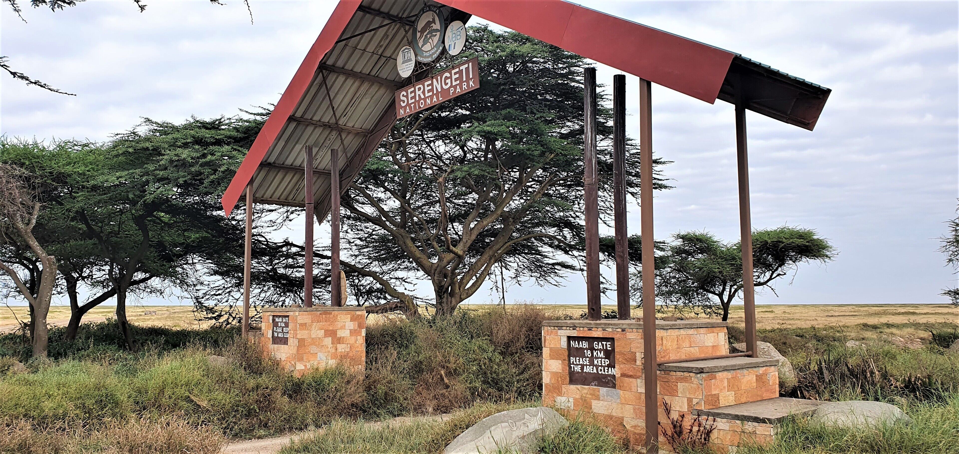 Un panneau indiquant le parc national du Serengeti, avec une structure à toit rouge et deux panneaux d’information.