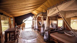A tented accommodation with a wooden floor, a round woven rug, and a bed with a canopy.