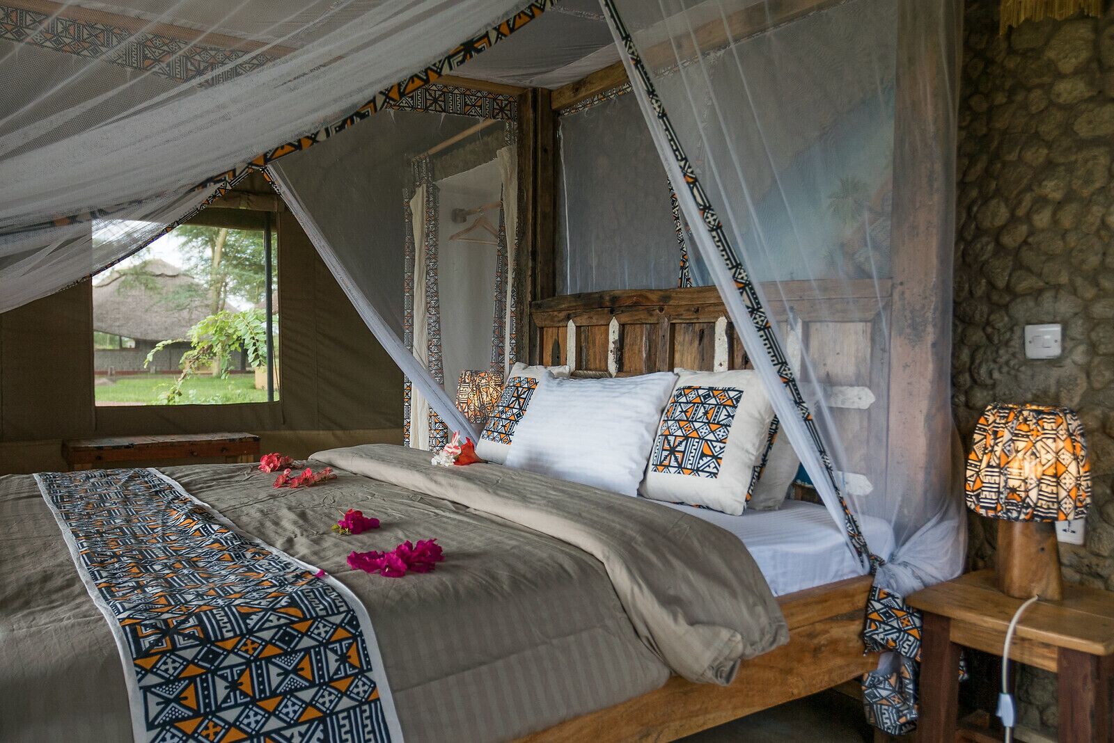 Una cama con dosel, una mesita de noche con lámpara y vistas al exterior.