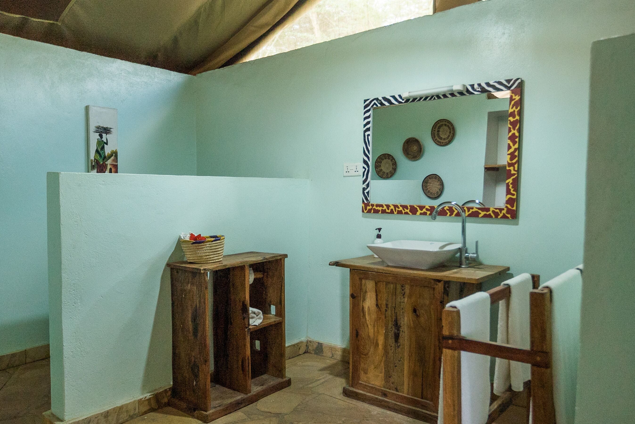 A bathroom with a wooden vanity, a sink, and a mirror with a decorative frame. There is a towel rack and a small shelf with a basket.