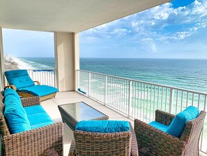 A balcony with wicker furniture and a glass table, overlooking a beach and ocean. - Stunning Corner-Unit, Miles of Coastal Views, Huge Balcony, Free Beach Chairs (Panama City Beach)