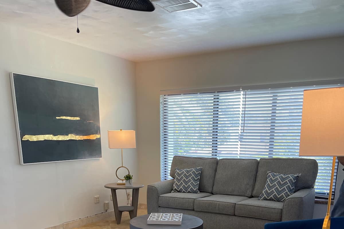 A modern living room with a grey sofa, a blue armchair, a round coffee table, and a large abstract painting on the wall.