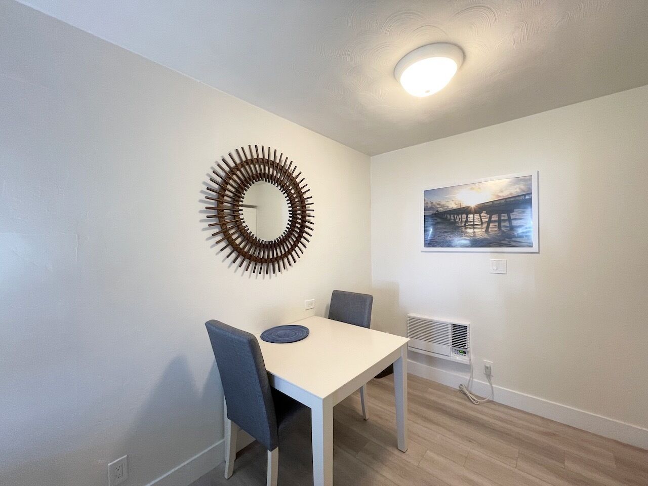 A dining area with a white table, two chairs, a decorative wall piece, and a framed picture on the wall.
