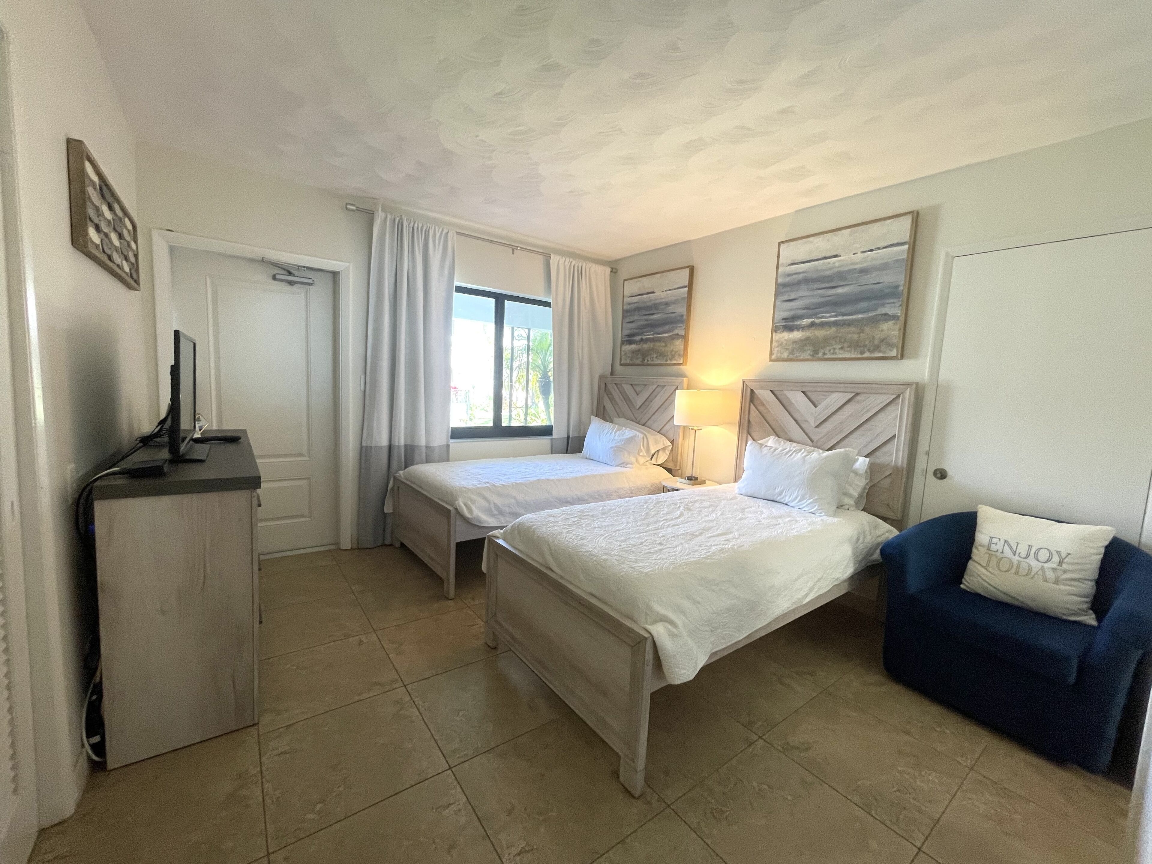A hotel room with two beds, a desk, a chair, and a window with curtains.