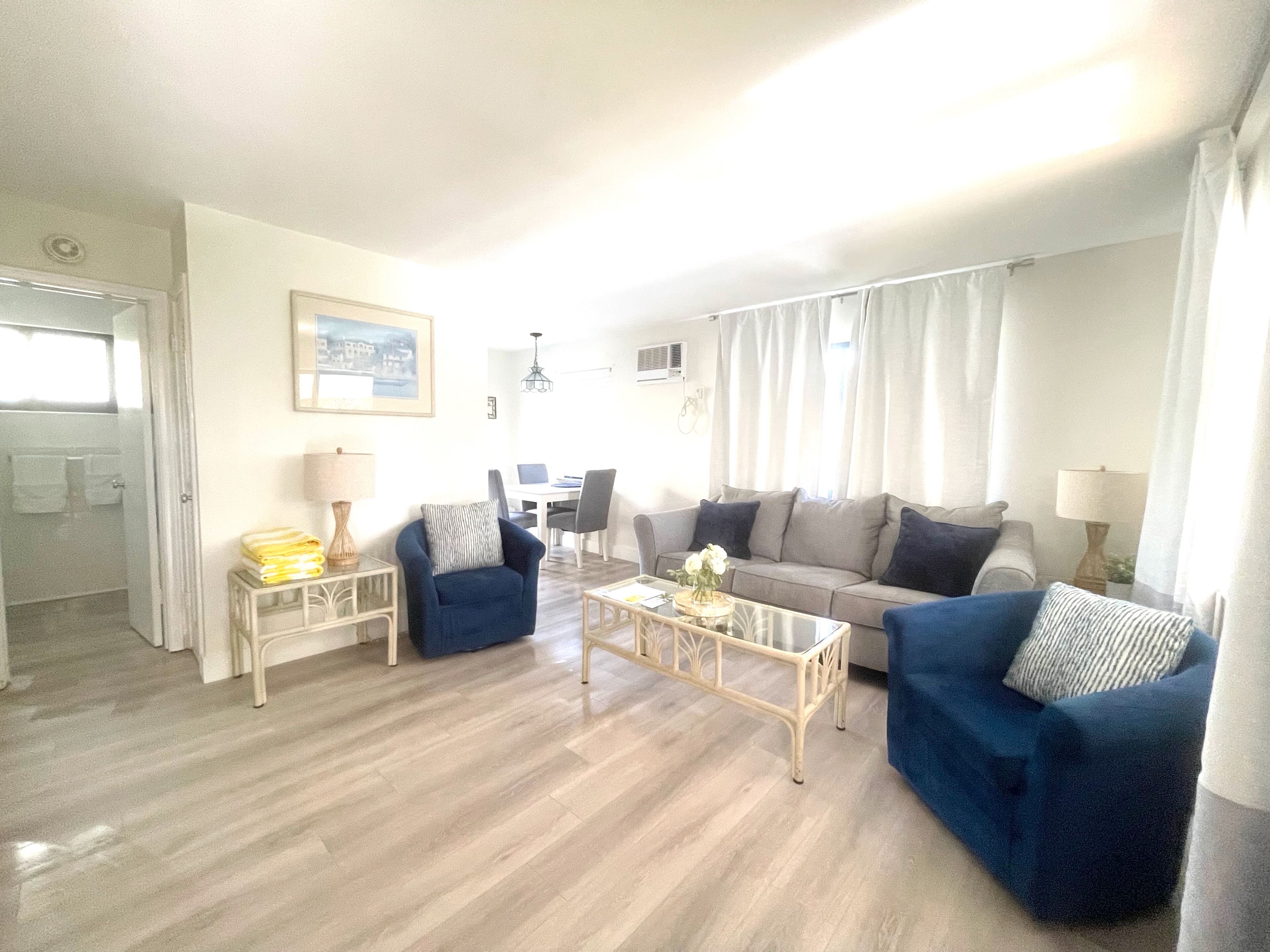 A living room with two blue sofas, a coffee table, and a dining area in the background.