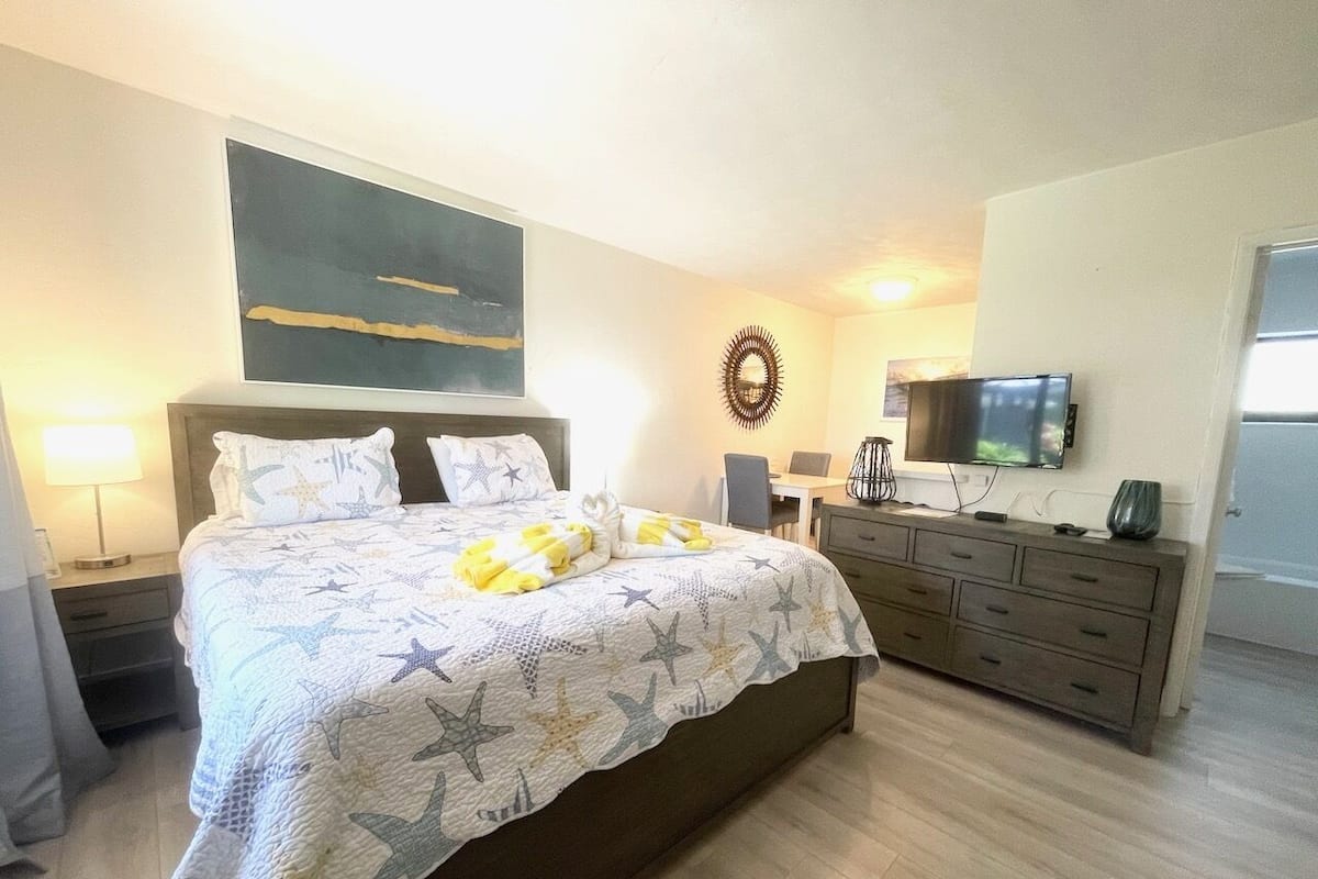 A hotel room with a bed, a desk, a dresser, a TV, and a wall art piece.