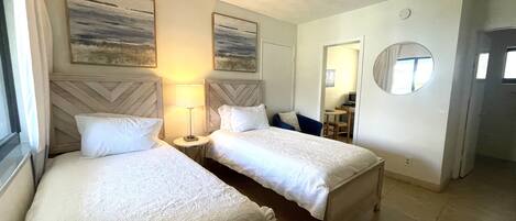 Een hotelkamer met twee bedden, een tafeltje, een lamp, een spiegel en kunst aan de muur.