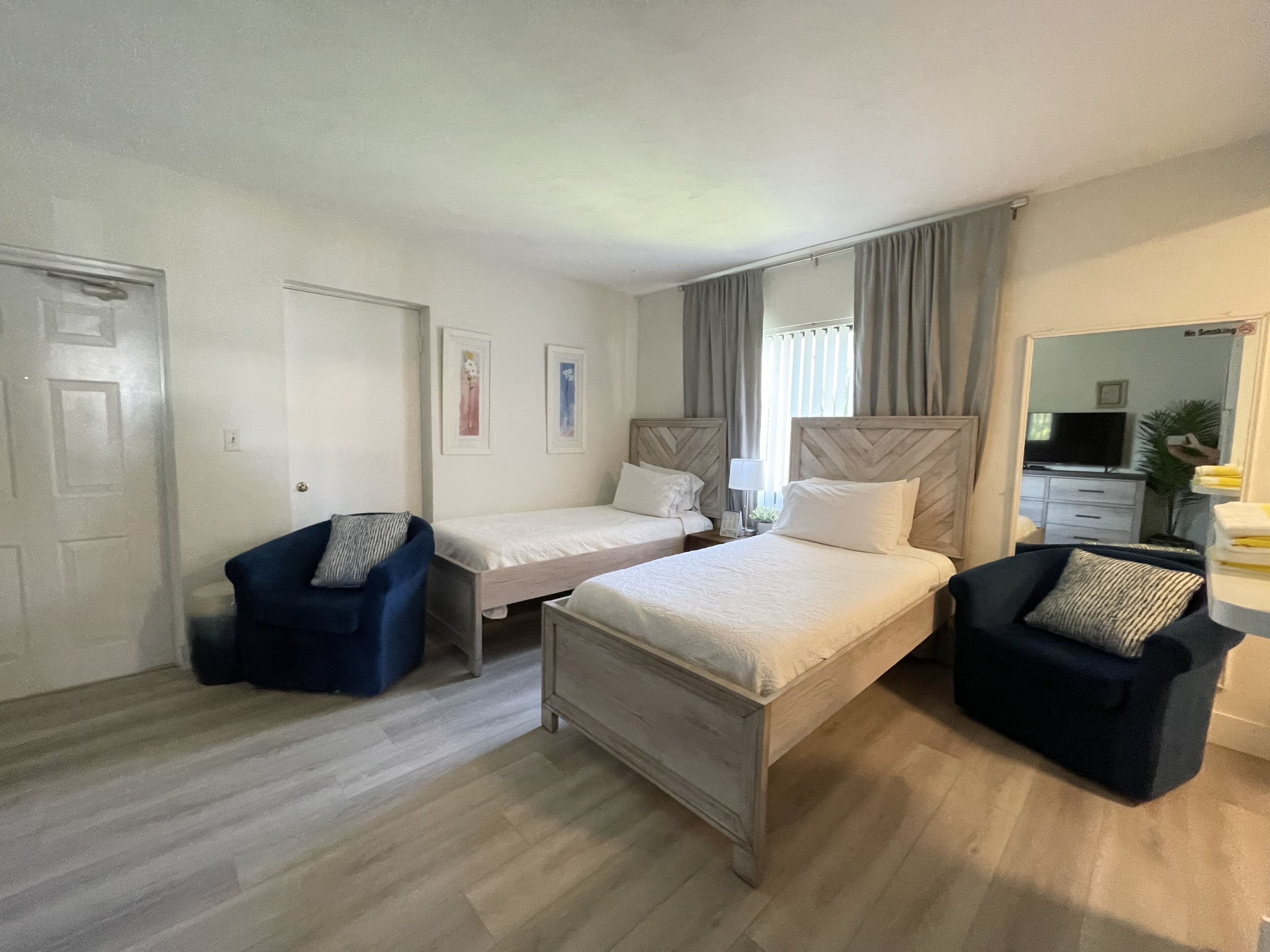 Ein Hotelzimmer mit zwei Einzelbetten, einem blauen Sessel, einem Holznachttisch und einem Fernseher.