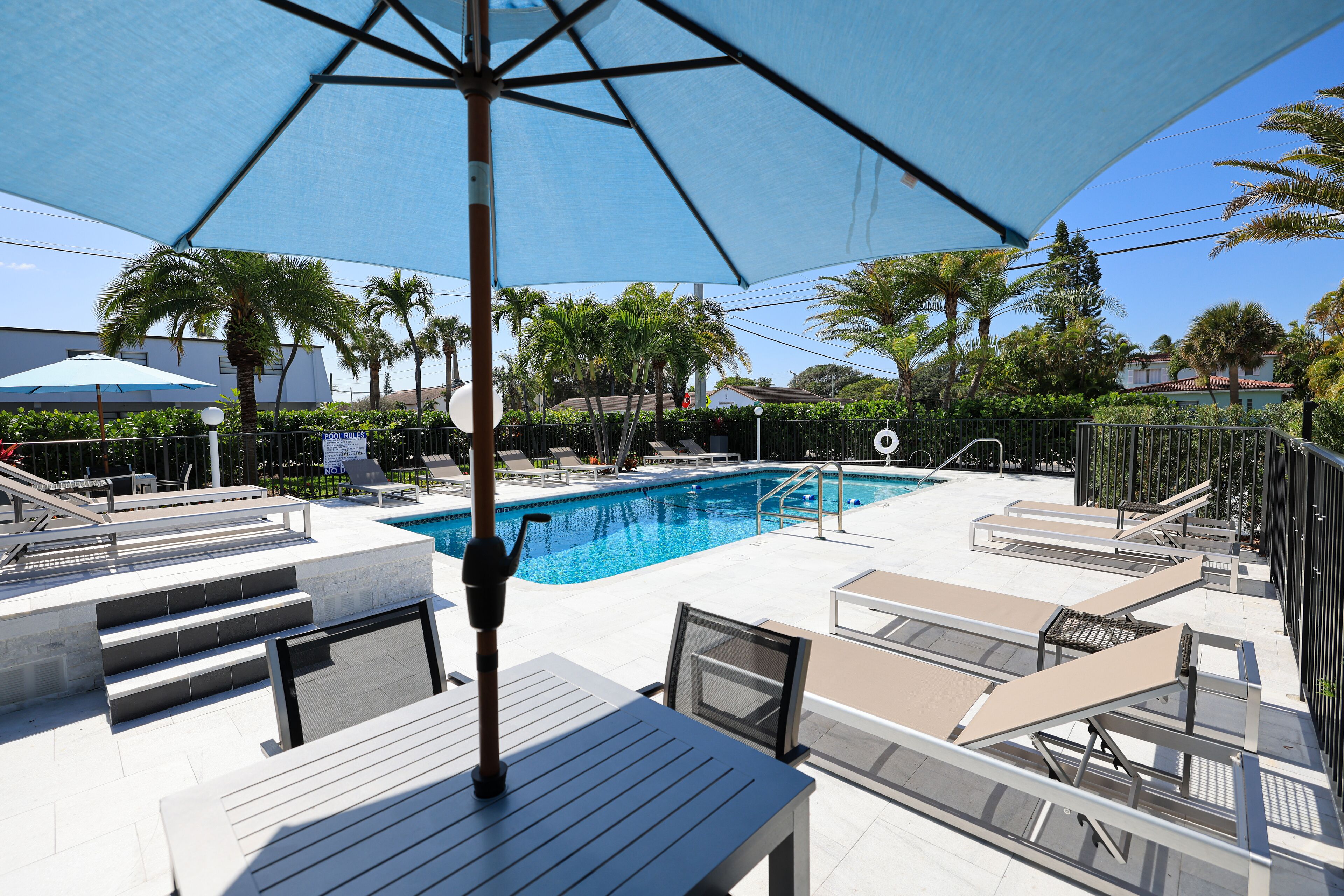 A poolside area with lounge chairs, a pool, and a large umbrella providing shade.