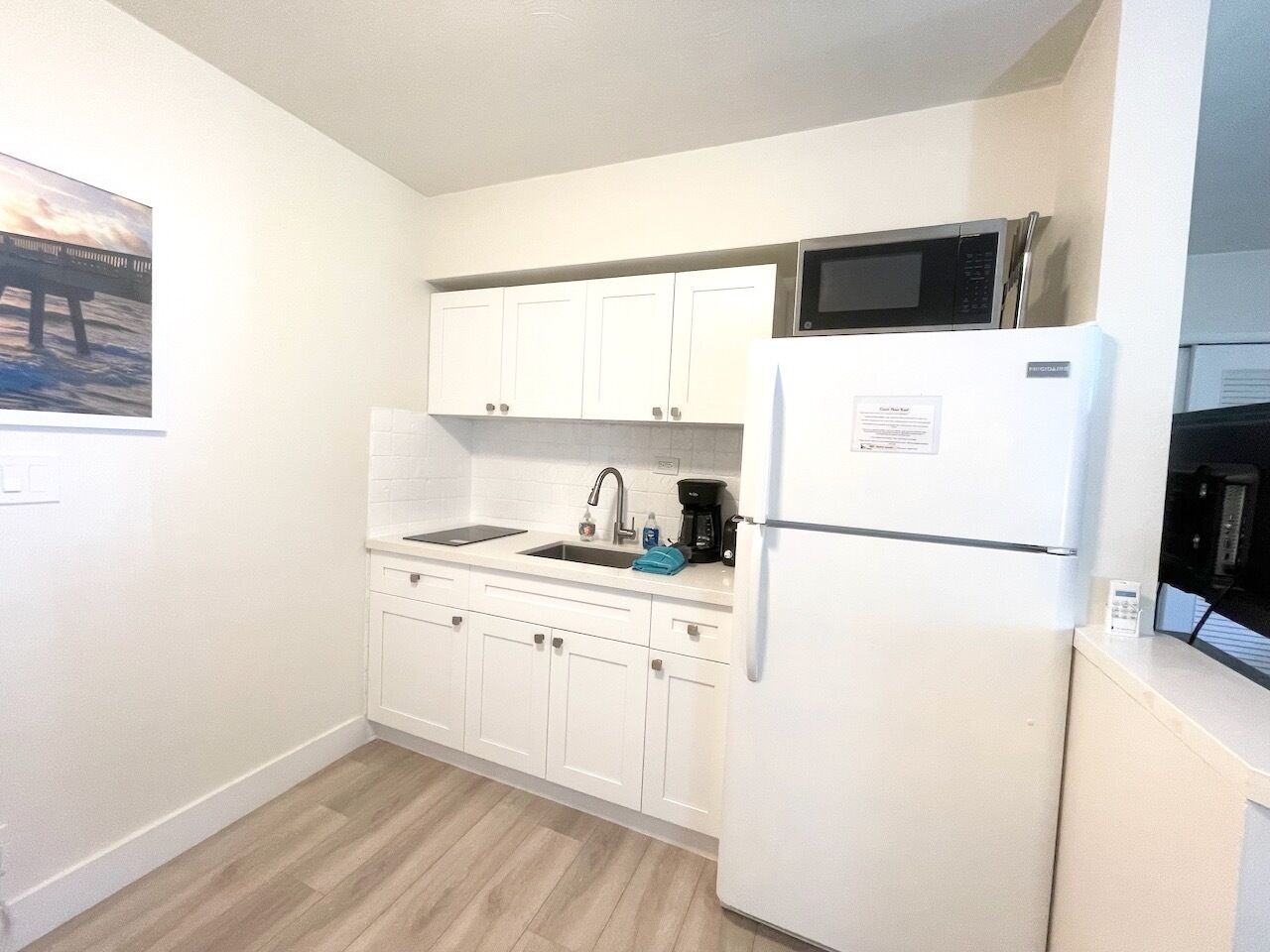 Una cocina compacta con armarios blancos, un microondas integrado, un refrigerador y un lavamanos.