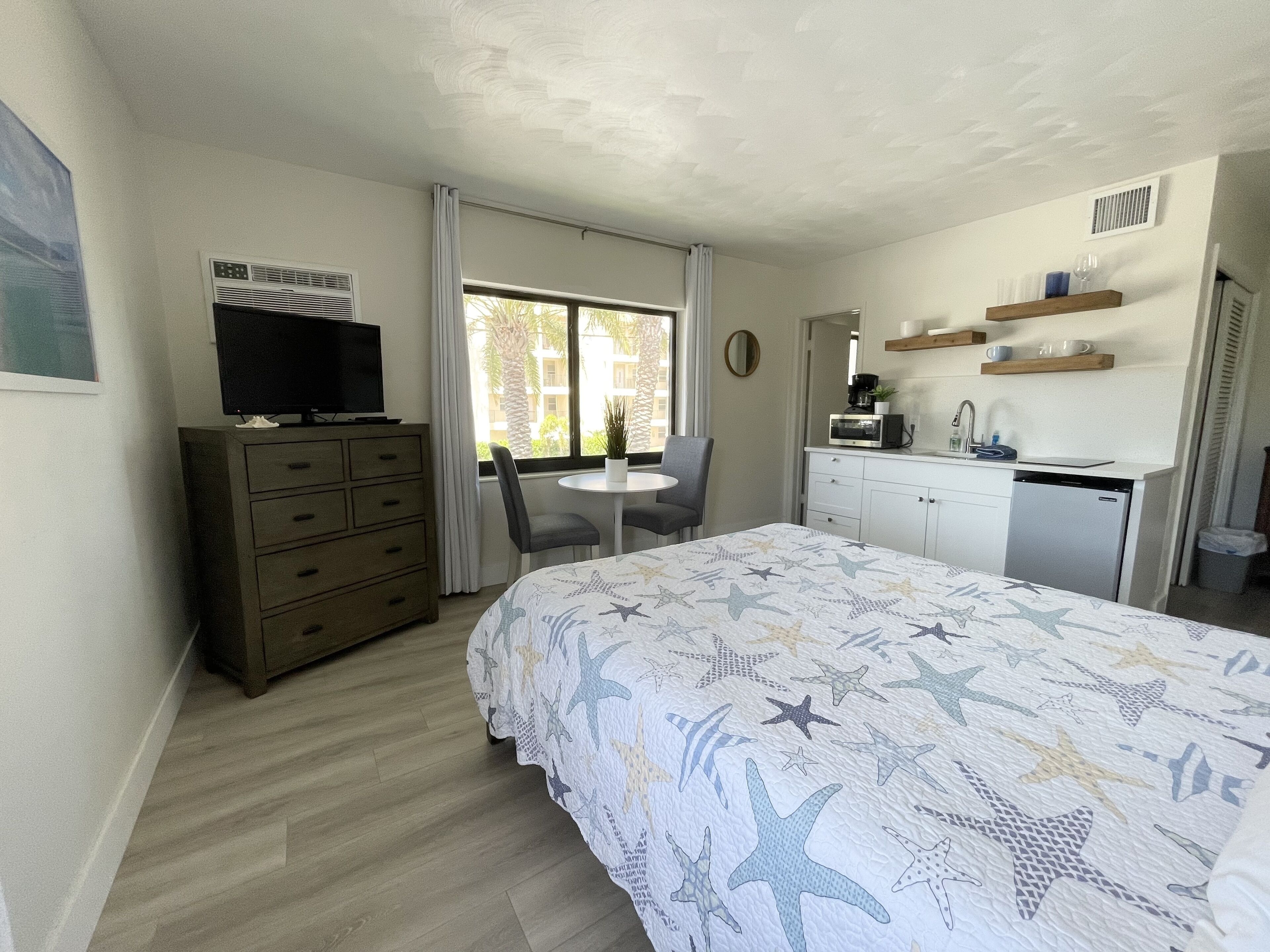 Ein gemütliches Hotelzimmer mit Bett, Fernseher auf einer Kommode, einem kleinen Esstisch und einer Küchenzeile.