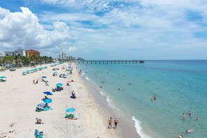 A beach with umbrellas, people, and a pier. - Tropic Isle Beach Resort (Deerfield Beach)