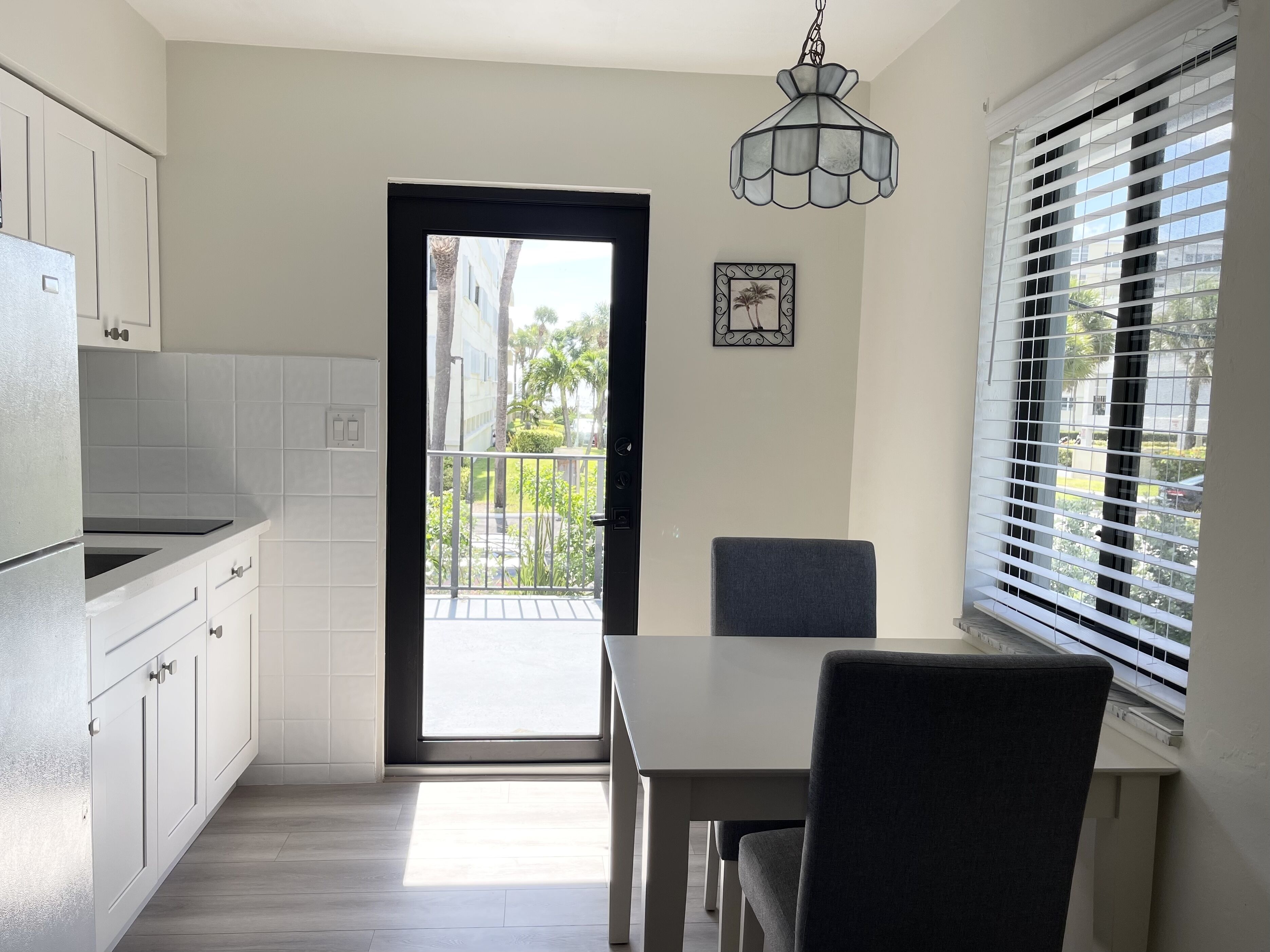A modern kitchen with white cabinets, a dining table, and a view of a balcony with a railing.
