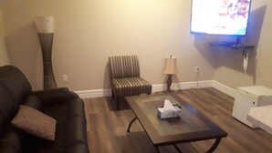 Een woonkamer met een donkergrijze bank, een gestreepte stoel, een salontafel met een zakdoekendoos, een lamp en een televisie aan de muur.
