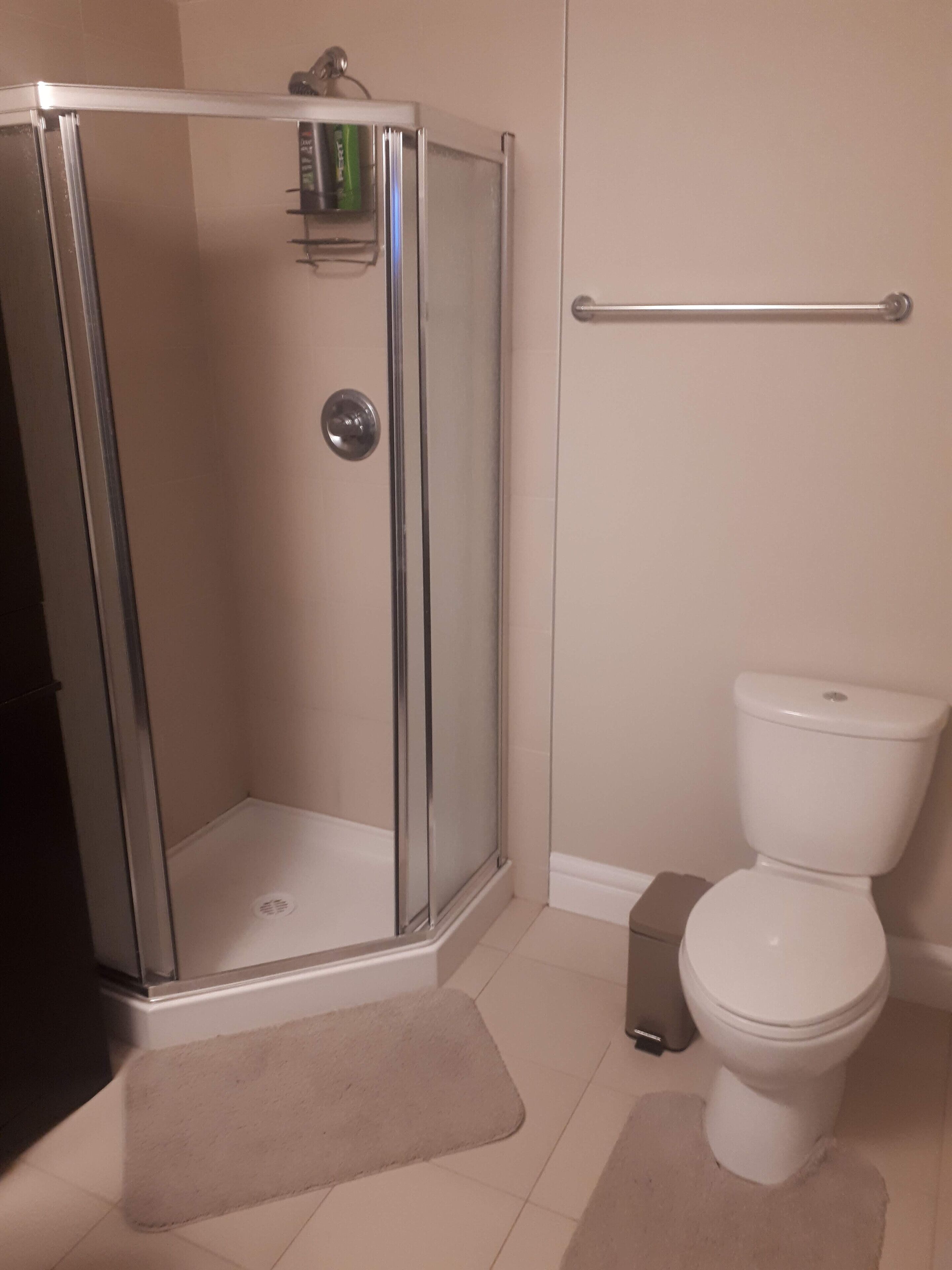 Un baño con ducha de vidrio, inodoro blanco y suelo color beige.