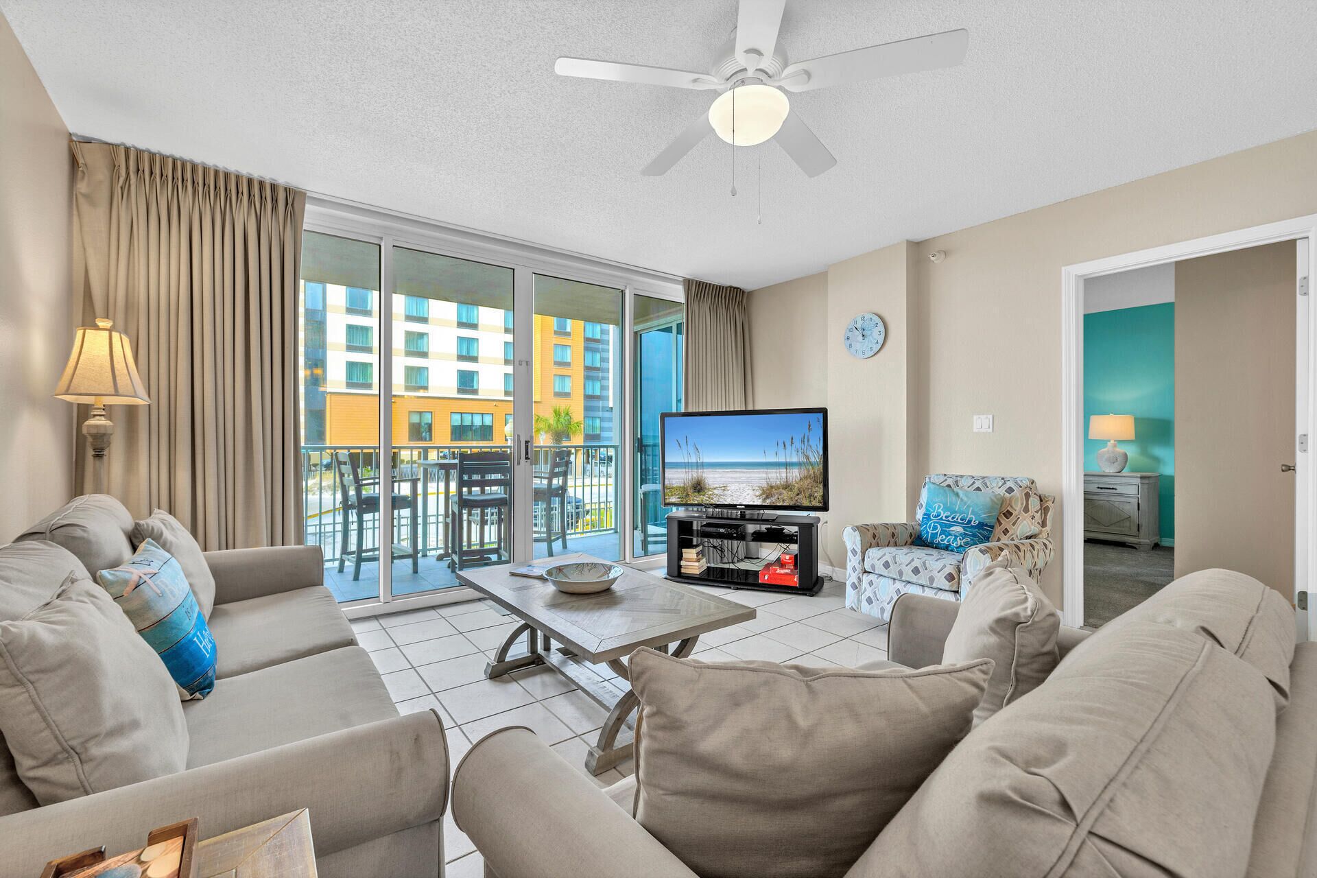 A living room with a television, sofa, and a balcony with a view of a building.