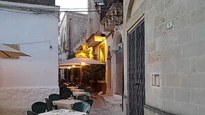 An outdoor dining area with tables and chairs, a covered seating area, and a building with a large door and window.