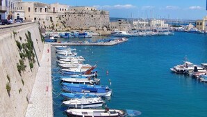 A harbor with numerous boats docked along a stone quay, a historic stone wall, and a clear blue sky.