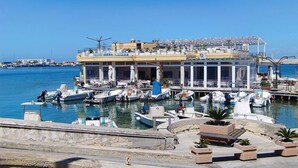 A marina with boats docked, a building with a balcony, and a clear sky.