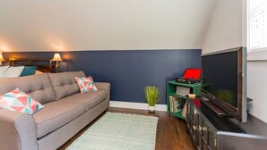 A living room with a sofa, a television, a small plant, and a bookshelf.