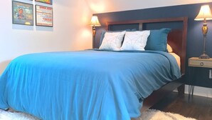 A bedroom with a large bed, two bedside lamps, and a wall with framed posters.