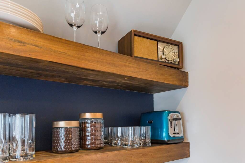 A kitchen shelf with a clock, jars, glasses, and a toaster.