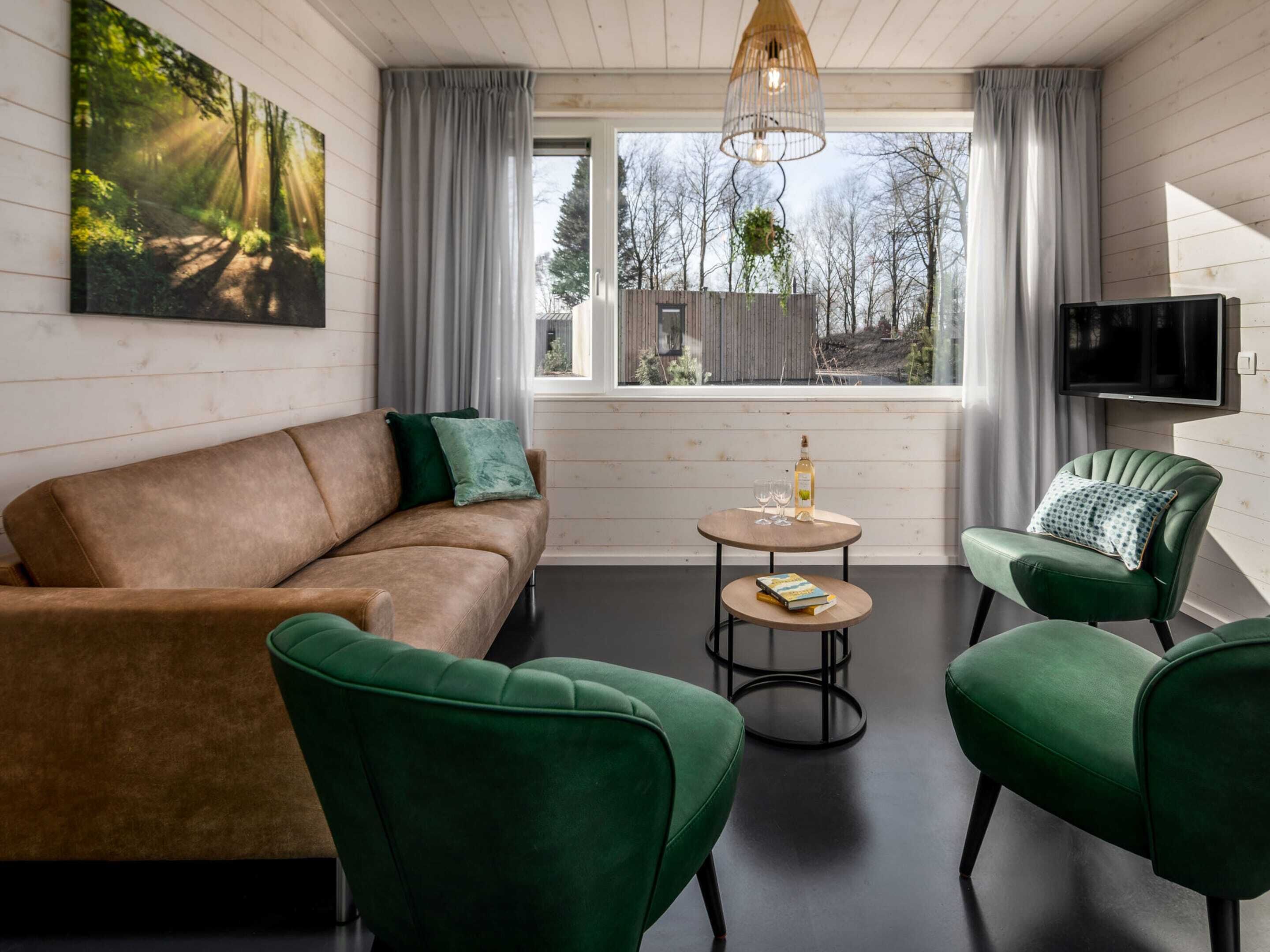 A modern living room with a sofa, two green armchairs, a small round table, and a TV mounted on the wall.