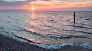 Ein Sonnenuntergang über einem ruhigen Meer mit sanften Wellen und wolkenlosem Himmel.