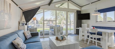 Ein modernes Wohnzimmer mit einem blauen Sofa, einem Essbereich mit weißem Tisch und Stühlen sowie großen Glasüren, die auf eine Terrasse führen.