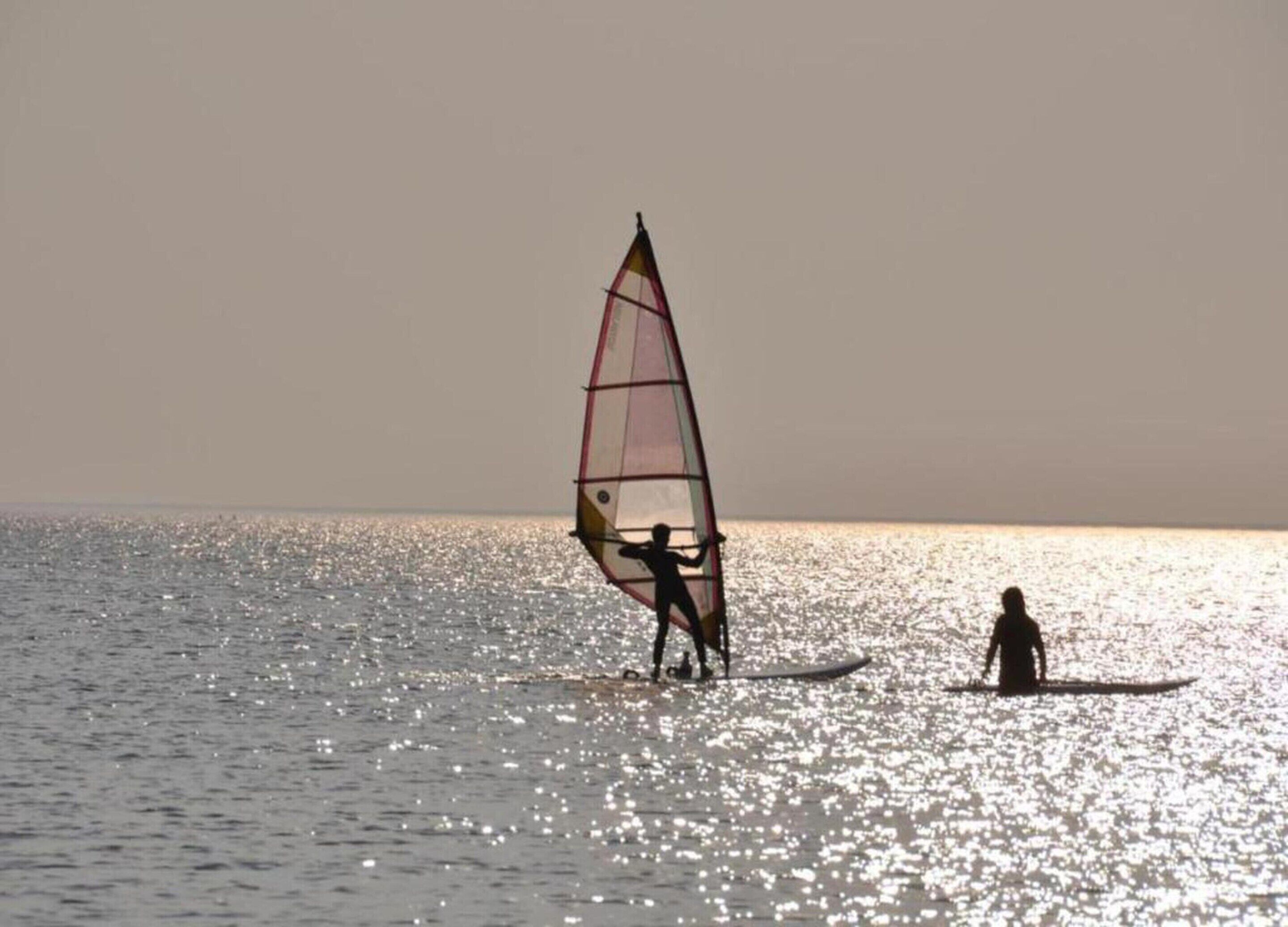 Eine Person windsurft auf ruhiger See mit klarem Horizont.