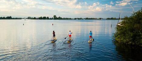 Tres personas haciendo paddleboard en un lago tranquilo con cielo despejado y barcos a la distancia.