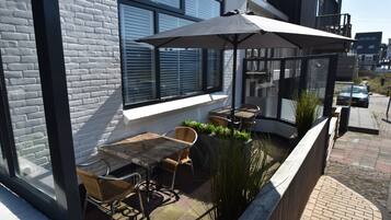 An outdoor patio with a table and chairs, a large umbrella, and a view of the street.