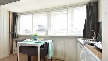 A compact kitchen with a dining area, a window with blinds, a radiator, and a washing machine.