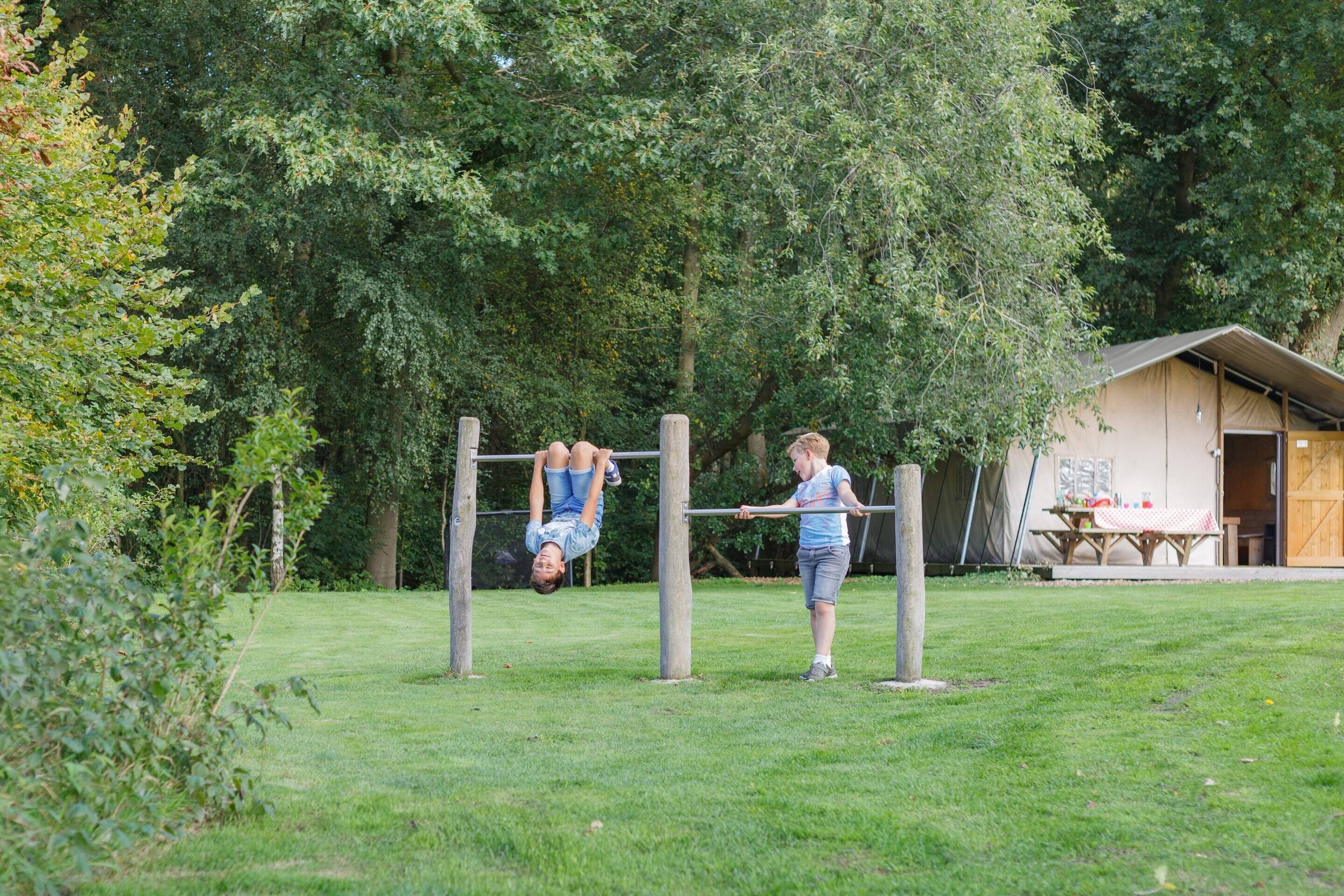 Un espacio al aire libre con césped, una estructura de madera, posiblemente una zona de juegos o equipamiento para ejercicio, y un edificio con una puerta y ventanas al fondo.