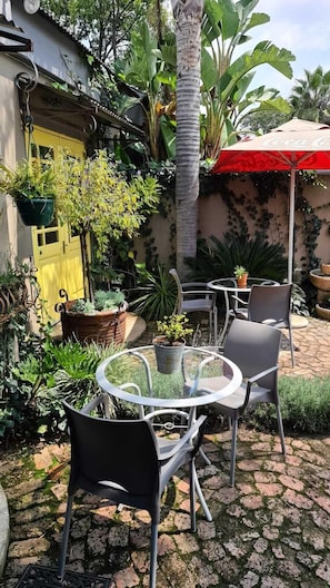 A patio with a glass table and chairs, surrounded by potted plants and a yellow door. - The Minimalist (Benoni)