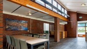 A spacious dining area with a long table and chairs, brick walls, and large windows. - Well Furnished Home for Groups with Fireplace near Water (Gasselternijveen)