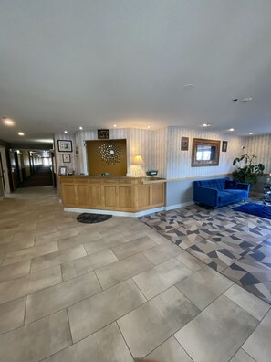 A hotel lobby with a reception desk, a blue sofa, patterned flooring, and a hallway leading to other rooms.