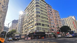 Edifício com vários andares e área comercial no térreo, incluindo uma vitrine com mesas ao ar livre.