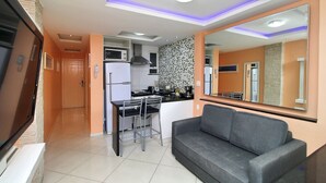 Uma cozinha moderna com uma ilha central, uma área de refeições com cadeiras e um sofá cinza.